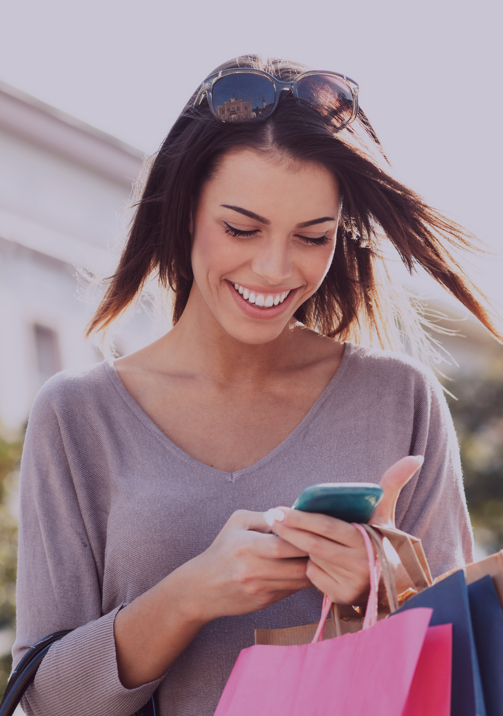 Young smiling woman with shopping bags, checking her wireless phone